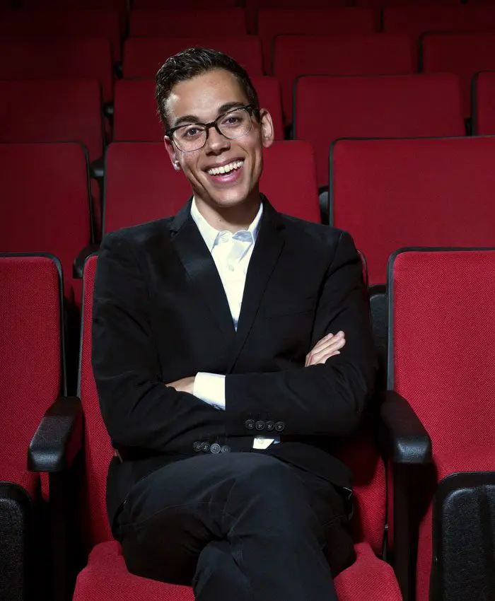 Evan Neff wearing black suit seated in movie theater with red seats